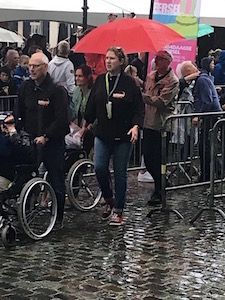 3e Rolstoel wandelevenement (een groep wandelaars inclusief mensen in rolstoel met duwer lopend in de regen met paraplu's